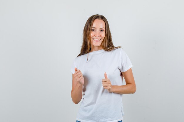 Молодая женщина в белой футболке, шортах показывает палец вверх и выглядит весело