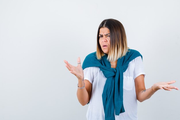 Young woman in white t-shirt spreading arms and looking resentful , front view.