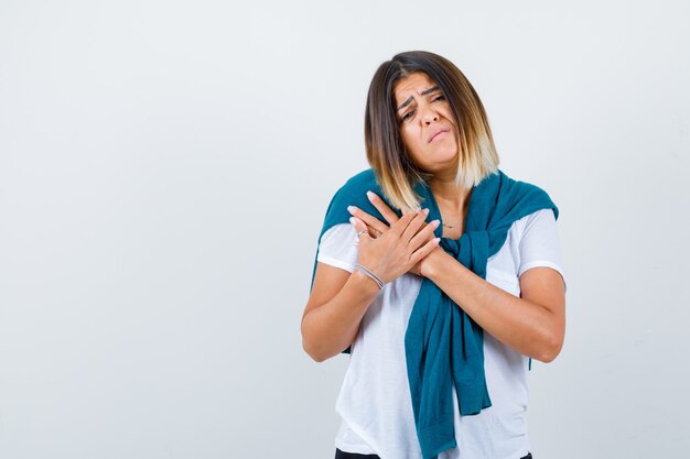 Young woman in white t-shirt with hands on chest and looking morose , front view.