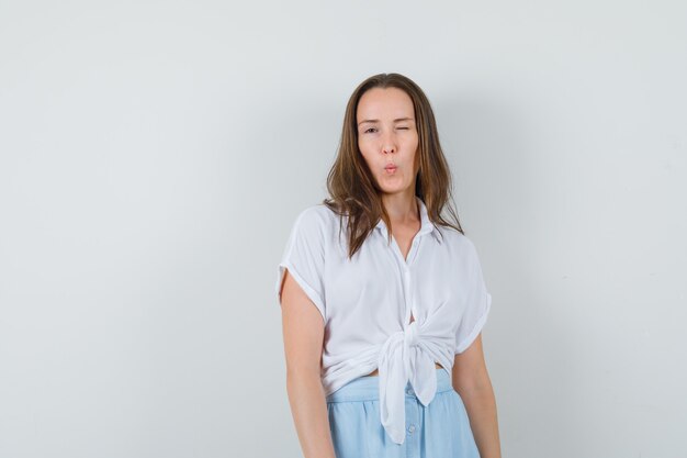 Young woman winking and posing at front in white blouse and light blue skirt and looking charming