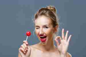 Free photo young woman winking, showing okay, holding lollipop