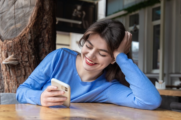 A young woman in wireless headphones uses the phone while sitting in a cafe