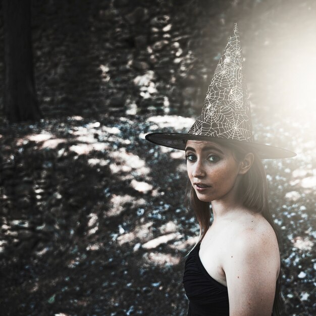 Young woman in witch hat looking at camera in forest