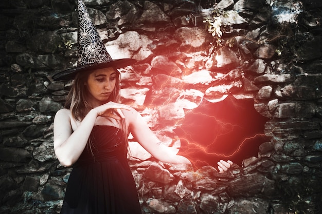 Young woman in witch hat showing magic with lightening