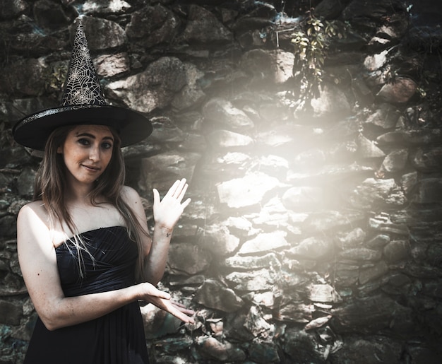 마녀 모자 벽에 밝은 자리 근처에 서있는 젊은 여자