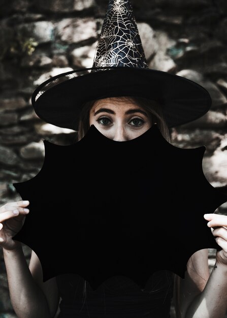 Young woman in witch hat with Halloween decoration looking at camera