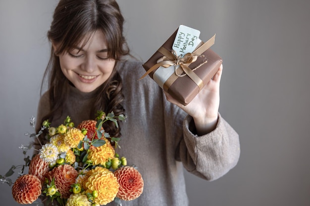 Молодая женщина с подарком на день матери и букетом цветов в руках