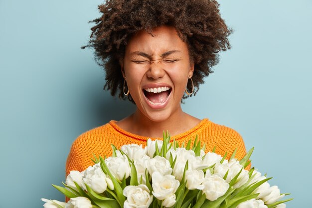 白い花の花束を保持しているアフロの散髪を持つ若い女性