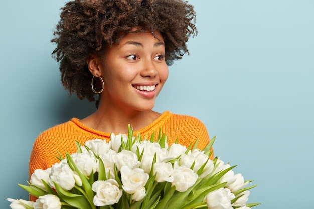 Giovane donna con taglio di capelli afro holding bouquet di fiori bianchi