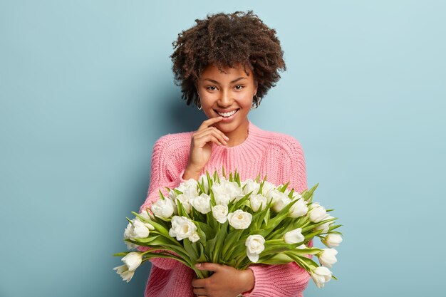 Young woman with Afro haircut holding bouquet of white flowers