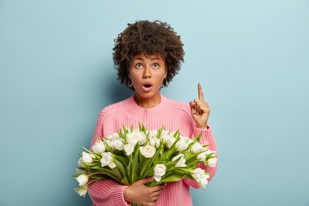 白い花の花束を保持しているアフロの散髪を持つ若い女性