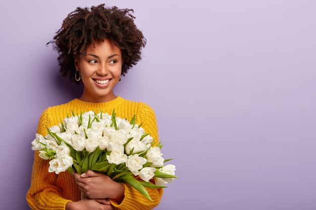Young woman with Afro haircut holding bouquet of white flowers