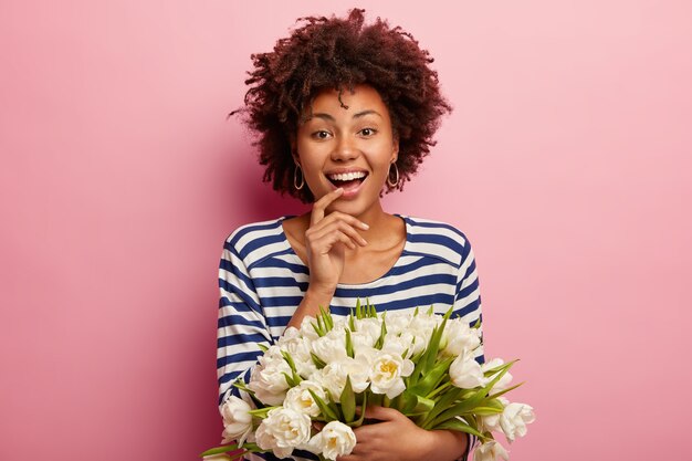 白い花の花束を保持しているアフロの散髪を持つ若い女性