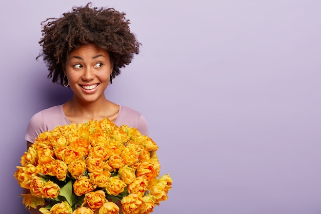 Free photo young woman with afro haircut holding bouquet of yellow flowers