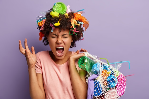 Giovane donna con taglio di capelli afro e rifiuti di plastica tra i capelli