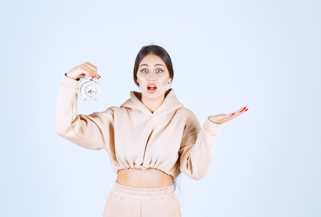 Young woman with an alarm clock looks terrified cause she is late