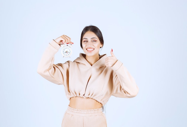 Young woman with an alarm clock showing good hand sign