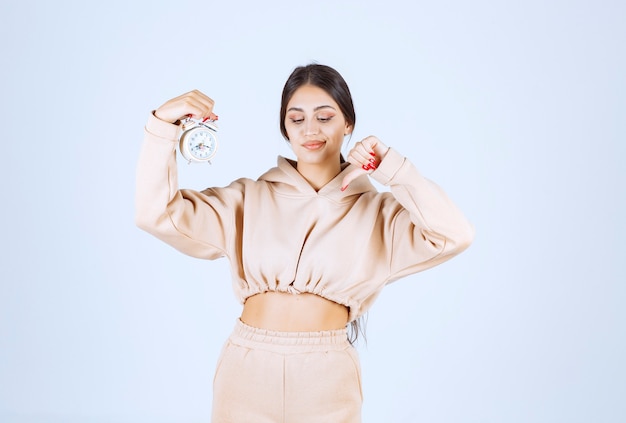 Free photo young woman with an alarm clock showing thumb down