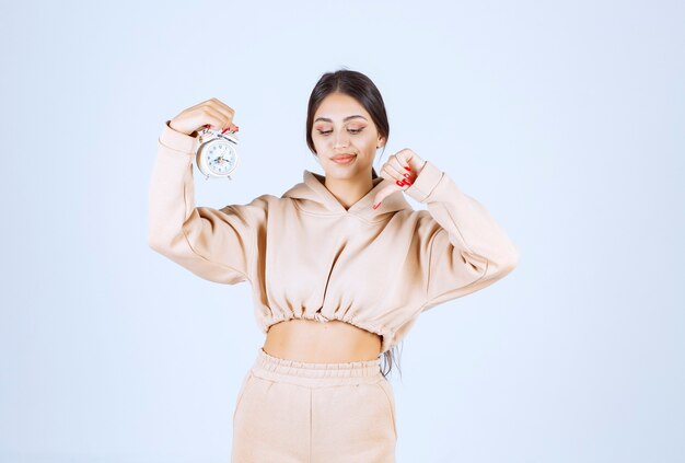 Young woman with an alarm clock showing thumb down