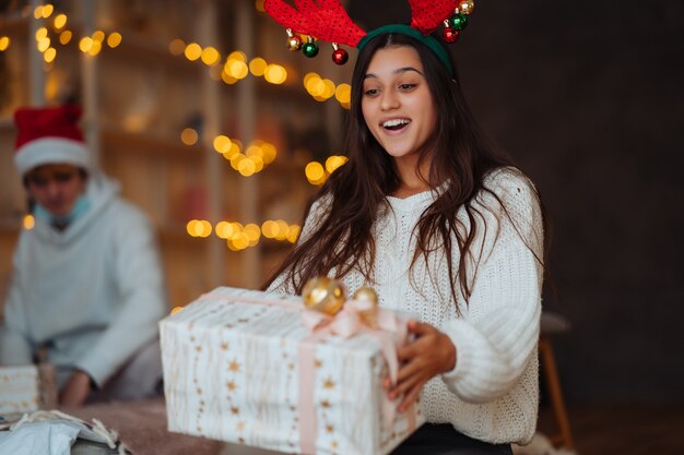 クリスマスのギフトボックスを開く枝角を持つ若い女性