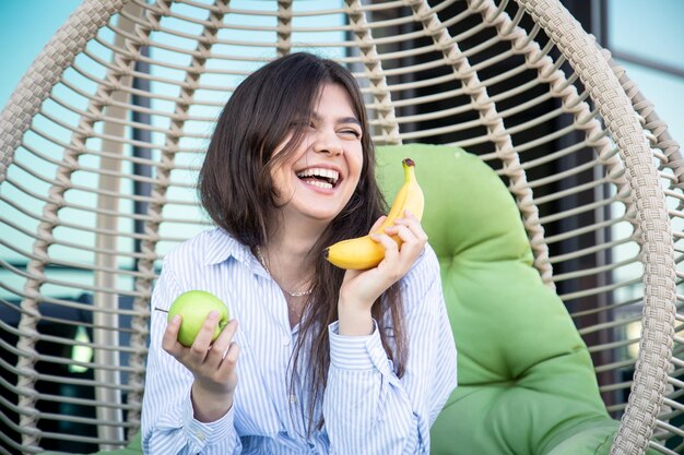 リンゴとバナナを持った若い女性がハンモックに座っている