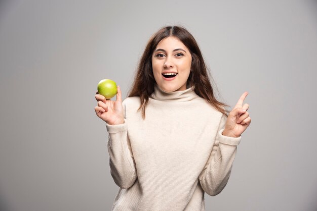 Young woman with an apple pointing up with an index finger.