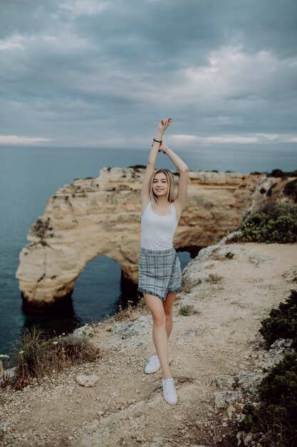 Young woman with arms wide open standing on rock in front of ocean beach on Portugal