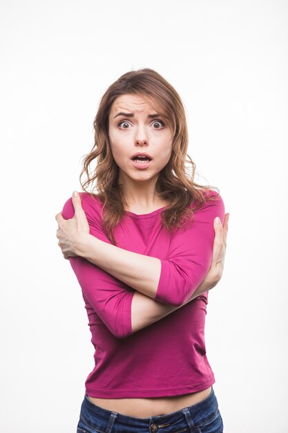 Young woman with astonished expression hugging herself against white background