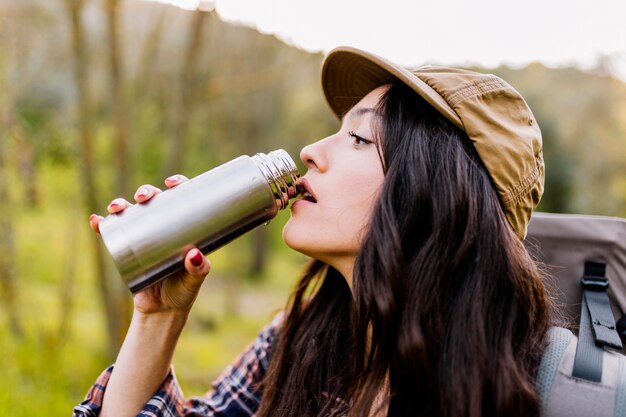 Young woman with backpack drinking from thermos