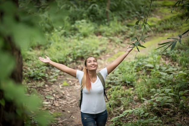 Free photo young woman with backpack and raised up arms while walking through the forest.