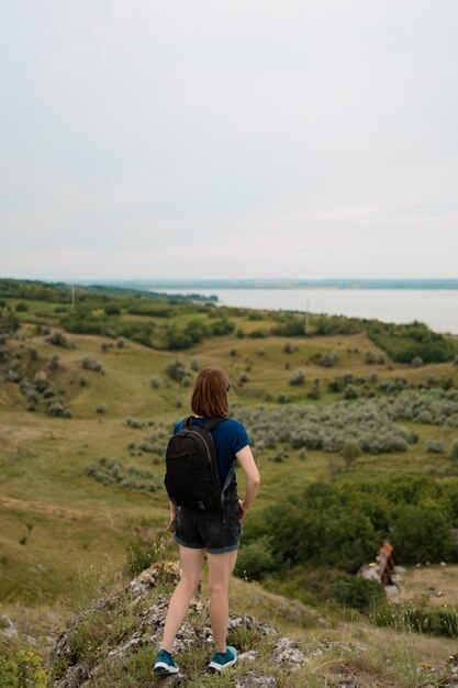 Young woman with backpack standing on cliff's edge and looking to the sky and beautiful nature.