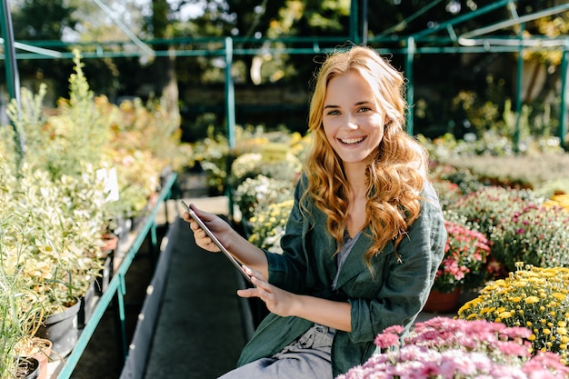 Young woman with beautiful blond hair and gentle smile, dressed in green robe with belt is working in greenhouse