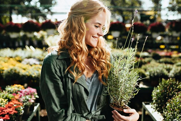 Young woman with beautiful blond hair and gentle smile, dressed in green robe with belt is working in greenhouse