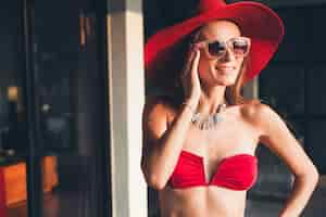 Foto gratuita giovane donna con un bel corpo snello che indossa costume da bagno bikini rosso, cappello di paglia e occhiali da sole che si distendono sul resort villa tropicale durante le vacanze in asia, figura magra, accessori di tendenza in stile estivo