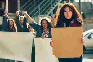 Foto gratuita giovane donna con poster in bianco di fronte a persone che protestano per i diritti delle donne e l'uguaglianza per strada.