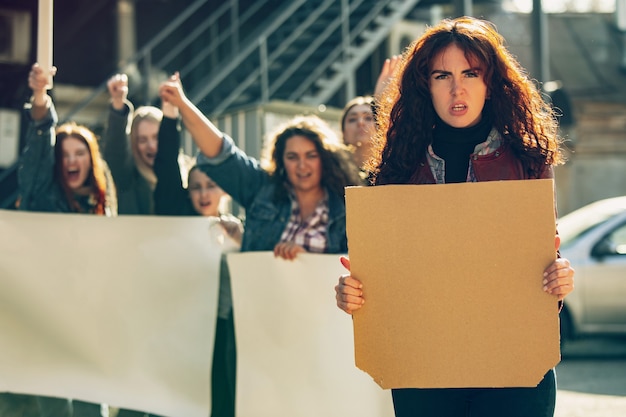 Young woman with blank poster in front of people protesting about women's rights and equality on the street.