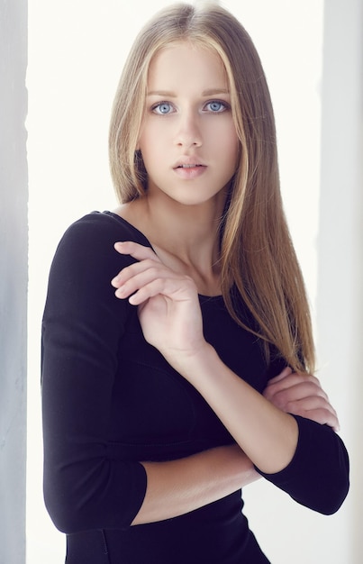 A young woman with blue eyes in a black dress with her arms crossed.