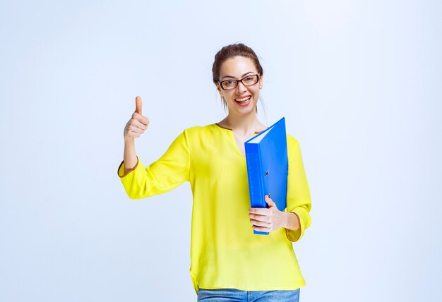 楽しさのサインを示す青いフォルダーを持つ若い女性