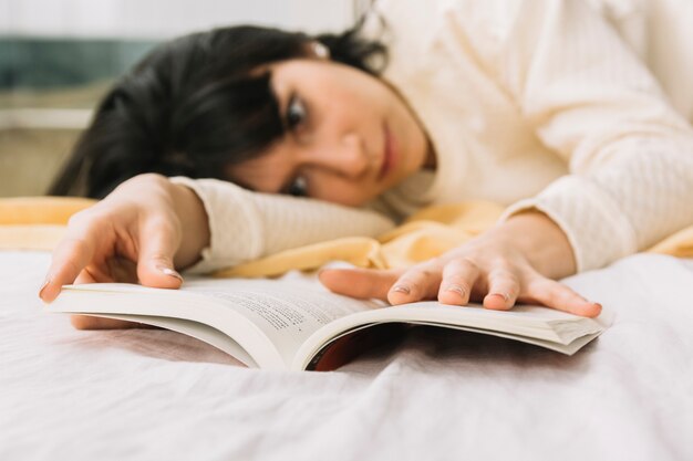 Young woman with book lying on bed