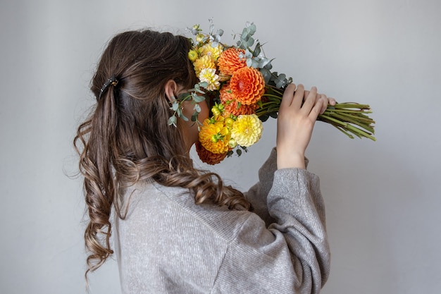 Young woman with a bouquet of fresh chrysanthemums on a gray background