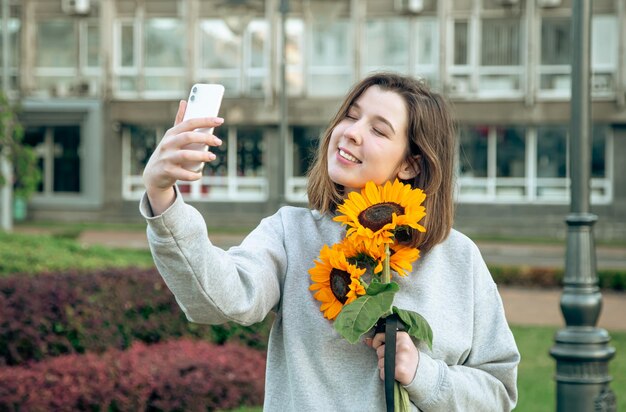 A young woman with a bouquet of sunflowers in the city takes a selfie