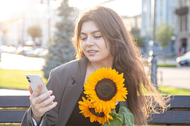 A young woman with a bouquet of sunflowers is talking on the phone at sunset