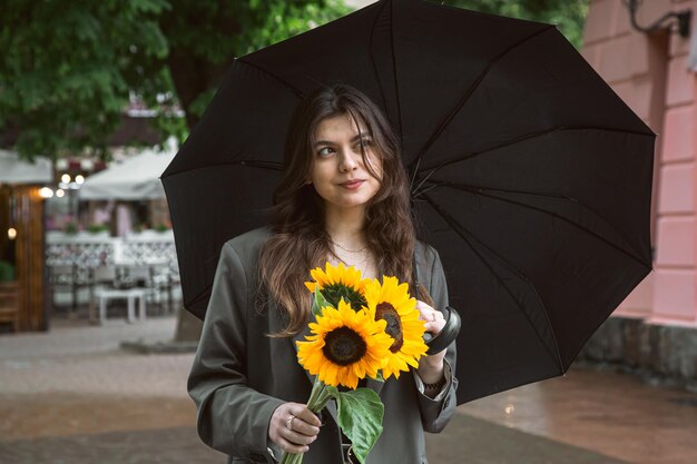 A young woman with a bouquet of sunflowers under an umbrella in rainy weather
