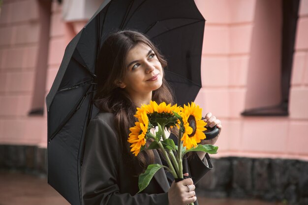 A young woman with a bouquet of sunflowers under an umbrella in rainy weather