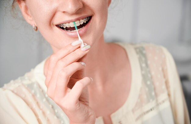 Young woman with braces on teeth using elastic cleaning toothpick