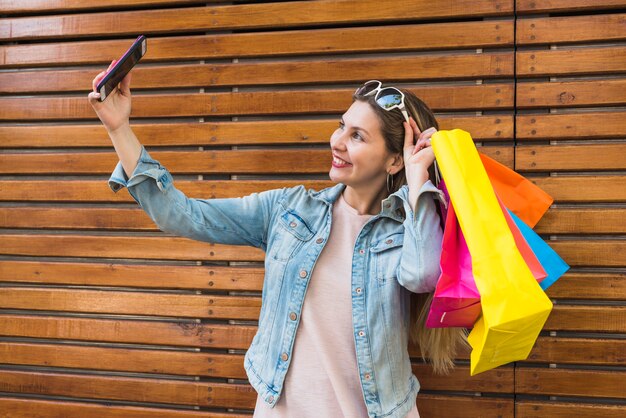 Young woman with bright shopping bags taking selfie