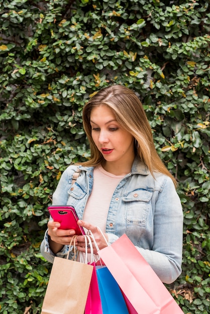 Young woman with bright shopping bags using smartphone outside