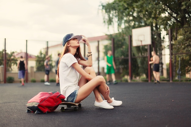 キャップとスケートボードを持つ若い女性