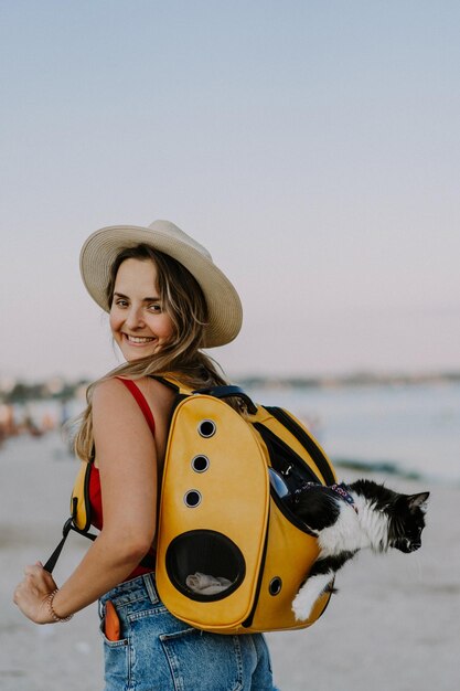 해변에 배낭에 고양이와 함께 아름 다운 젊은 여자. 애완 동물과 함께 여행 개념입니다. 현창이 있는 배낭 속의 고양이.