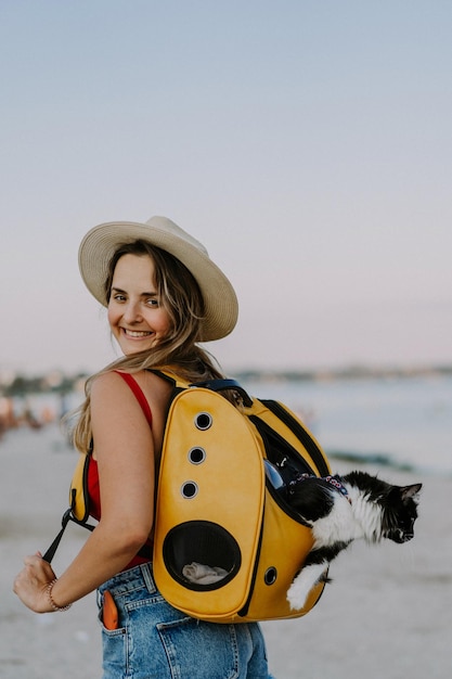 молодая женщина с кошкой в рюкзаке на берегу моря. Концепция путешествия с домашним животным. Кот в рюкзаке с иллюминатором.